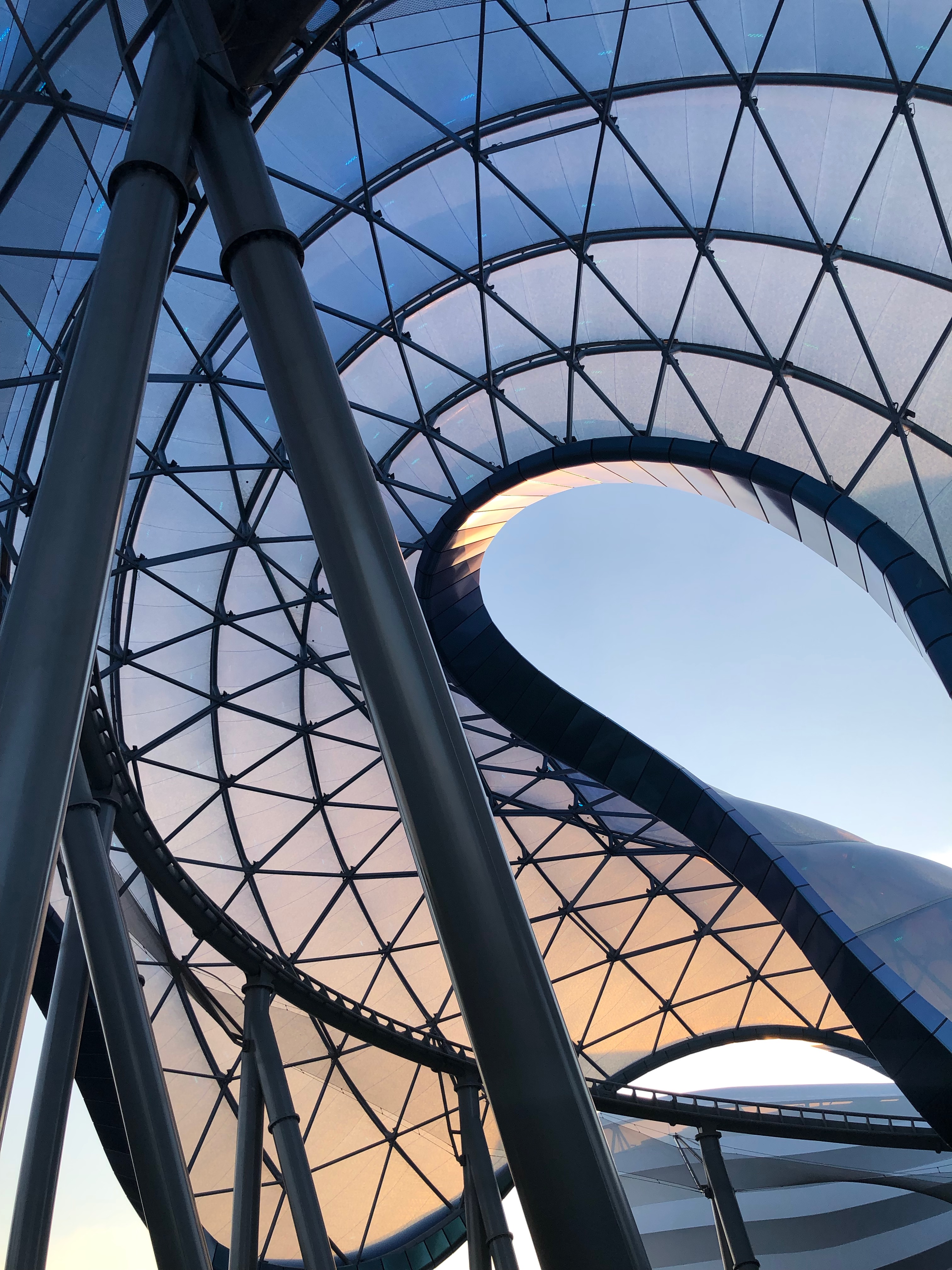 A photograph of a sinuous modern structure of glass and steel. The entrance to TRON Lightcycle Power Run features one of the most spectacular architectural spaces in a Disney theme park.