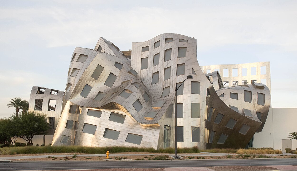 A uniquely designed building with an undulating metal facade and irregularly shaped windows, surrounded by trees and a street lamp. Photo of the Lou Ruvo Center by Monster4711 via [Wikimedia](https://commons.wikimedia.org/w/index.php?curid=36823235)