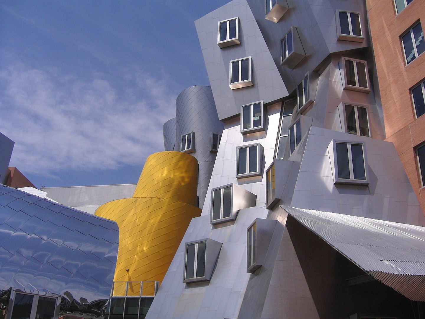 Abstract modern architecture featuring angular buildings with reflective surfaces in silver and yellow, against a blue sky backdrop. Photo of the Stata Center at MIT via [Wikimedia](https://en.wikipedia.org/w/index.php?curid=14118241)